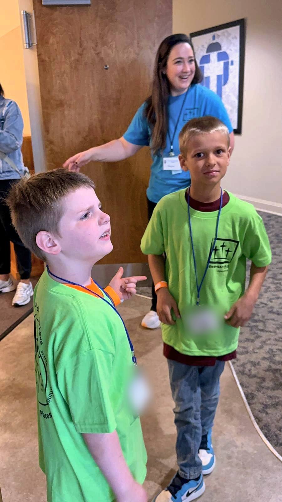 Two boys in green camp shirts with a laughing volunteer