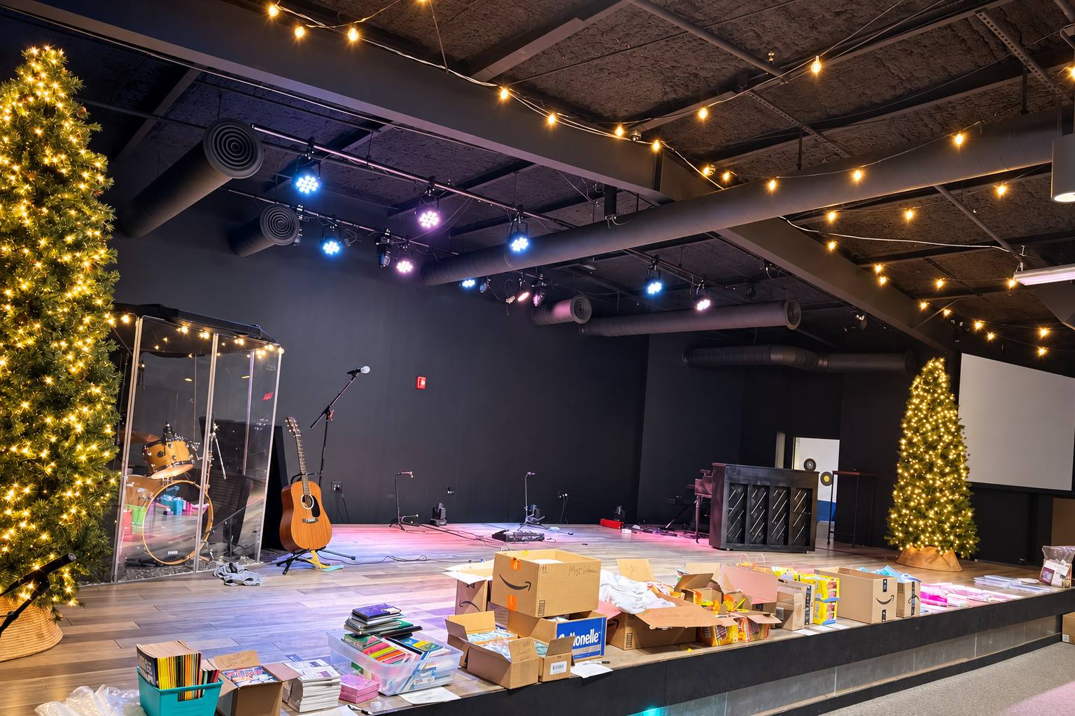 A church stage lit with string lights and Christmas trees, covered in donated supplies