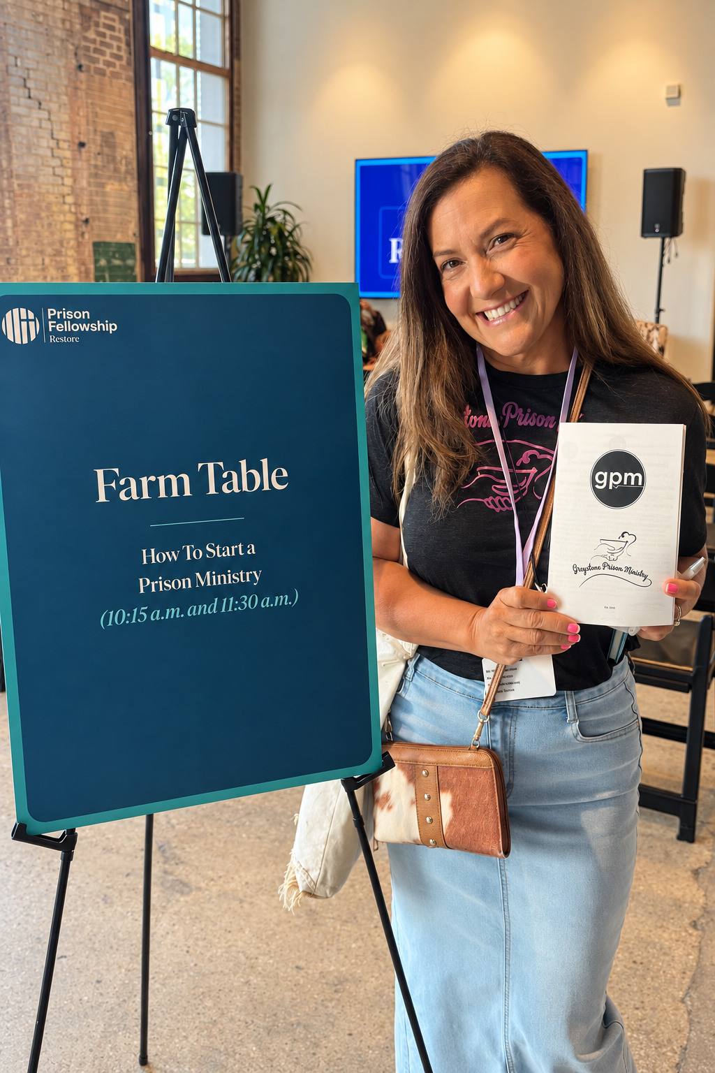 Marisol holding the GPM handbook beside a Prison Fellowship sign reading “Farm Table: How to Start a Prison Ministry”