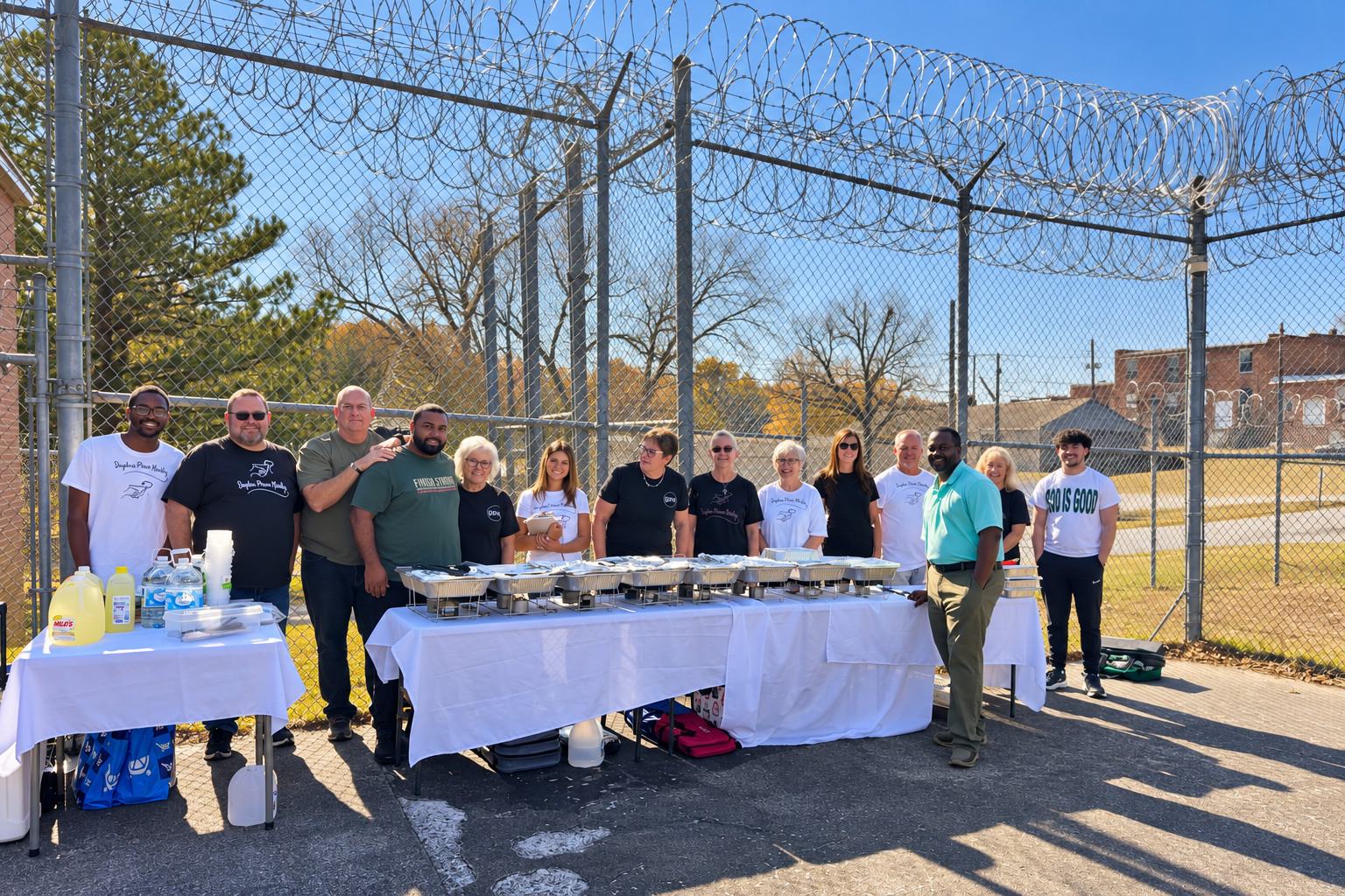 GPM volunteers behind a Thanksgiving serving line in the yard at Lincoln County Jail, razor wire against a blue sky